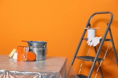 Photo of Can with paint, brush and renovation equipment on table against orange background