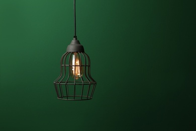 Hanging lamp bulb in chandelier against green background, space for text