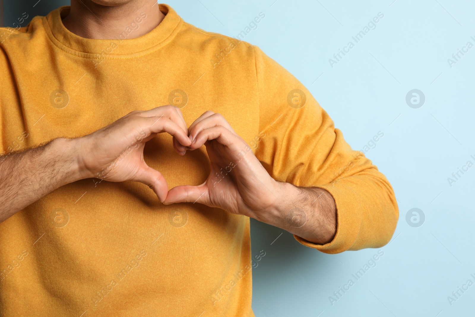 Photo of Man making heart with hands on light blue background, closeup