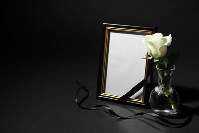 Photo of Funeral photo frame with ribbon and white rose on black background. Space for design