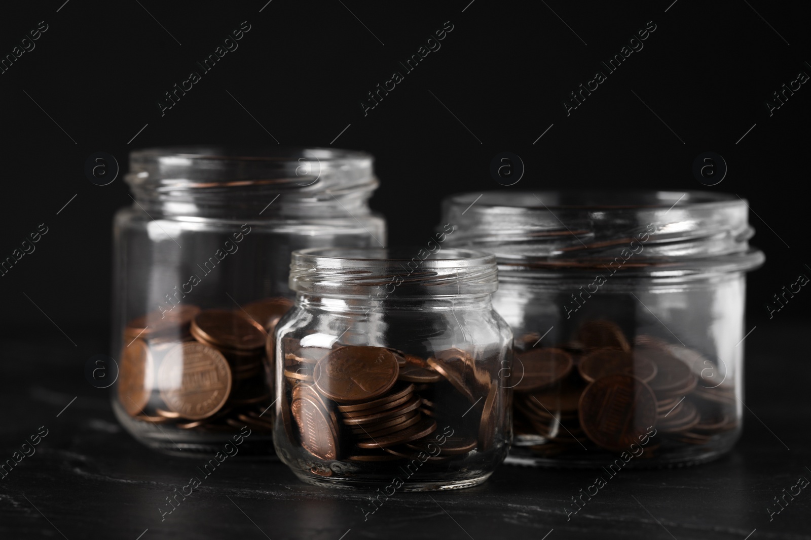 Photo of Glass jars with coins on black marble table, closeup