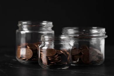 Photo of Glass jars with coins on black marble table, closeup