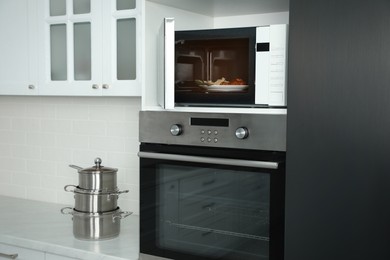 Photo of Open microwave oven with food on white shelf in kitchen