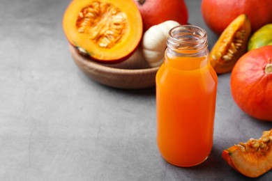 Photo of Tasty pumpkin juice in glass bottle and different pumpkins on light grey table. Space for text