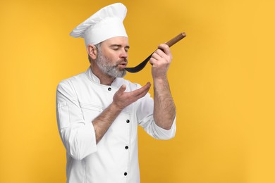 Photo of Chef in uniform tasting something on orange background