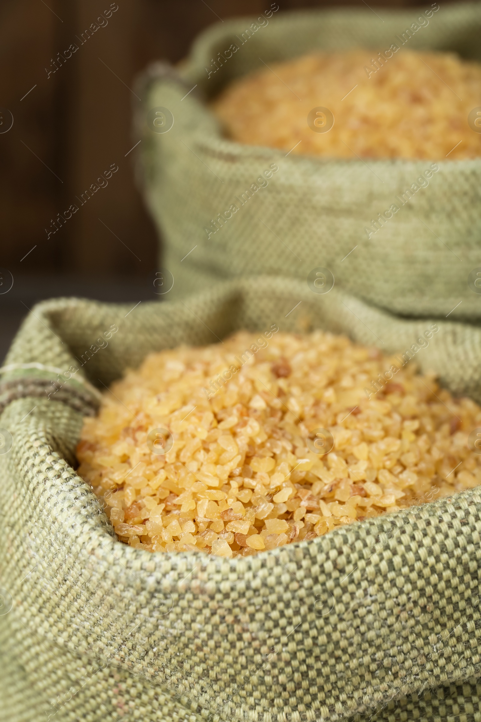 Photo of Burlap bags with uncooked bulgur on wooden background, closeup