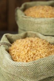 Burlap bags with uncooked bulgur on wooden background, closeup