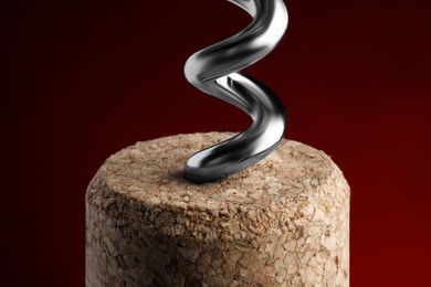 Photo of Corkscrew with cork against dark red background, closeup