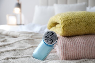 Modern fabric shaver and woolen sweaters on bed indoors, closeup. Space for text