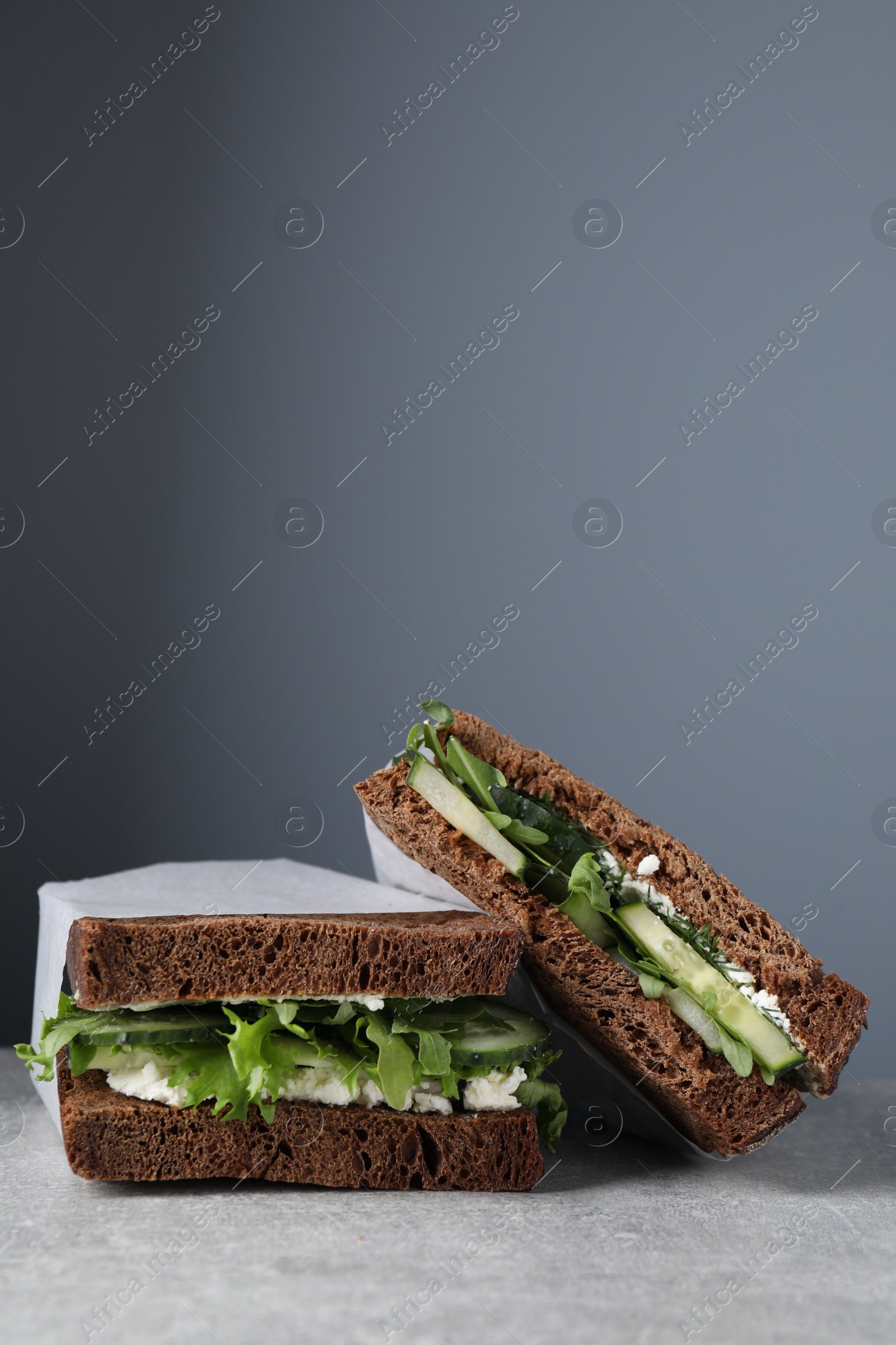 Photo of Tasty sandwiches with cream cheese, cucumber and greens on light grey table