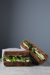 Tasty sandwiches with cream cheese, cucumber and greens on light grey table