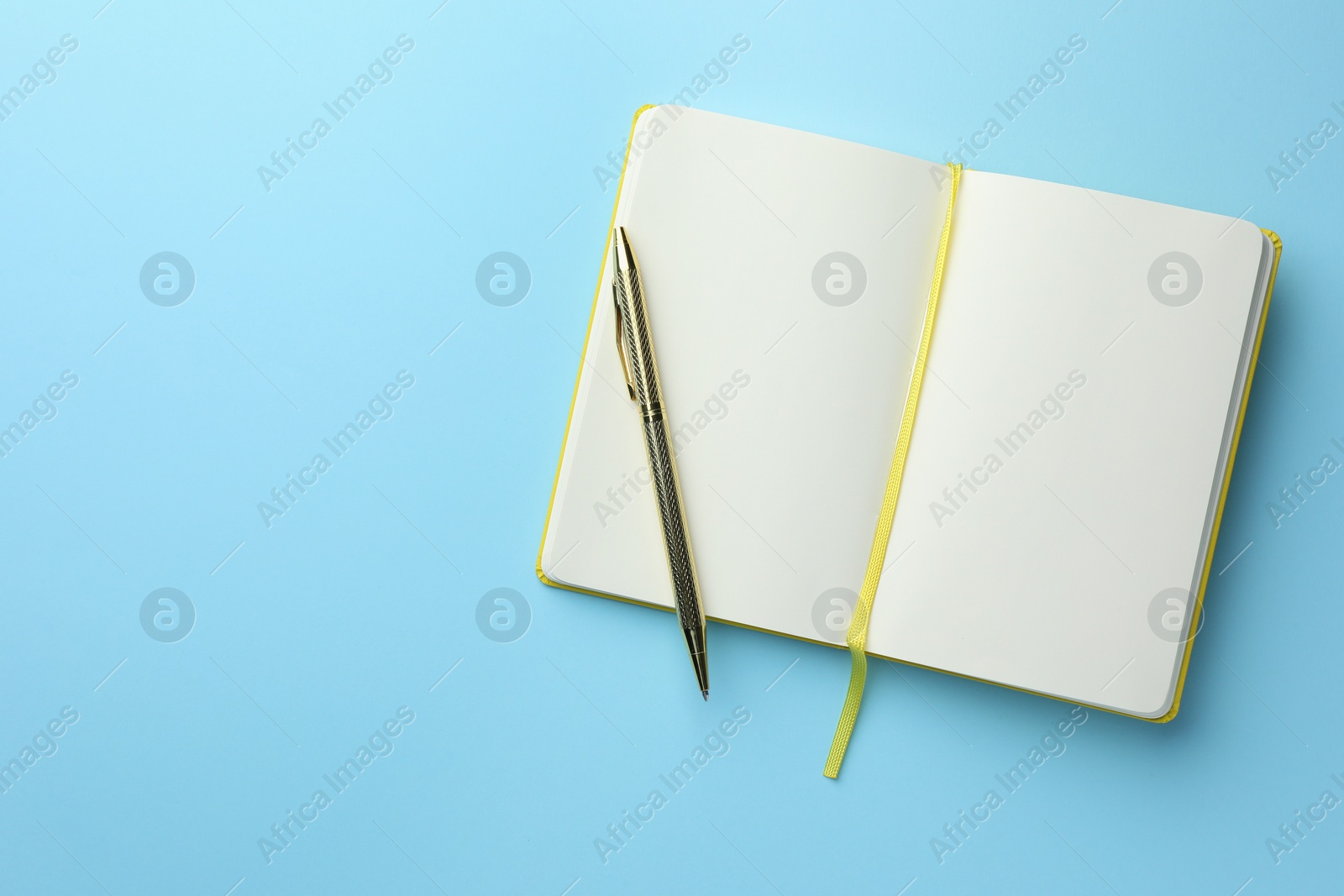 Photo of Open notebook with blank pages and pen on light blue background, top view. Space for text