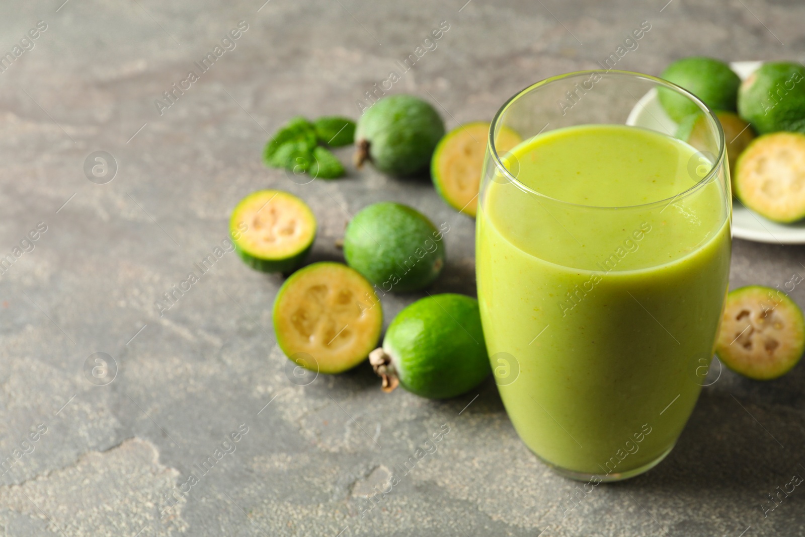 Photo of Fresh feijoa smoothie in glass on grey table, closeup. Space for text