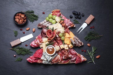 Photo of Fir tree shaped board with different appetizers and sauce on black table, flat lay