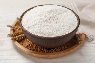 Photo of Bowl with organic flour, grains of wheat and spikelets on white wooden table, closeup