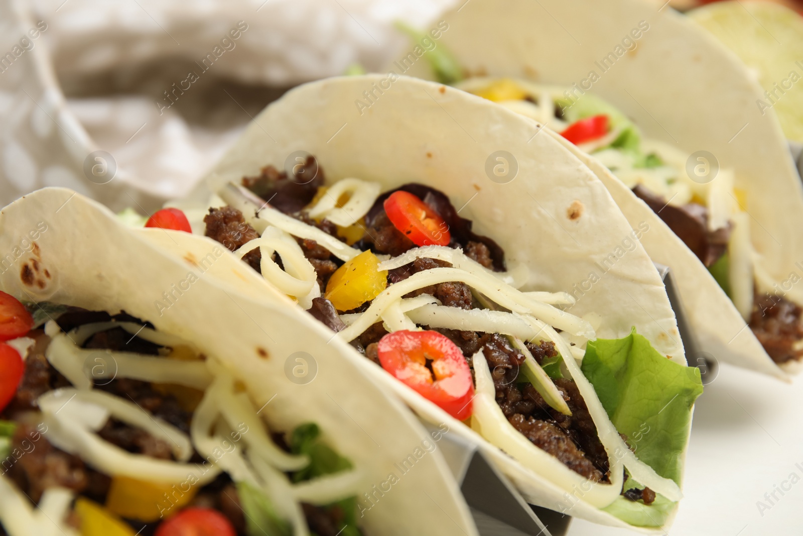 Photo of Delicious tacos with fried meat, vegetables and cheese on white table, closeup