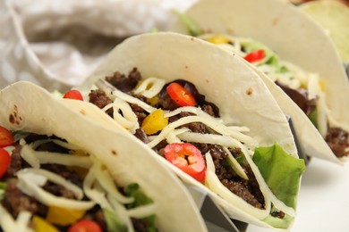 Photo of Delicious tacos with fried meat, vegetables and cheese on white table, closeup