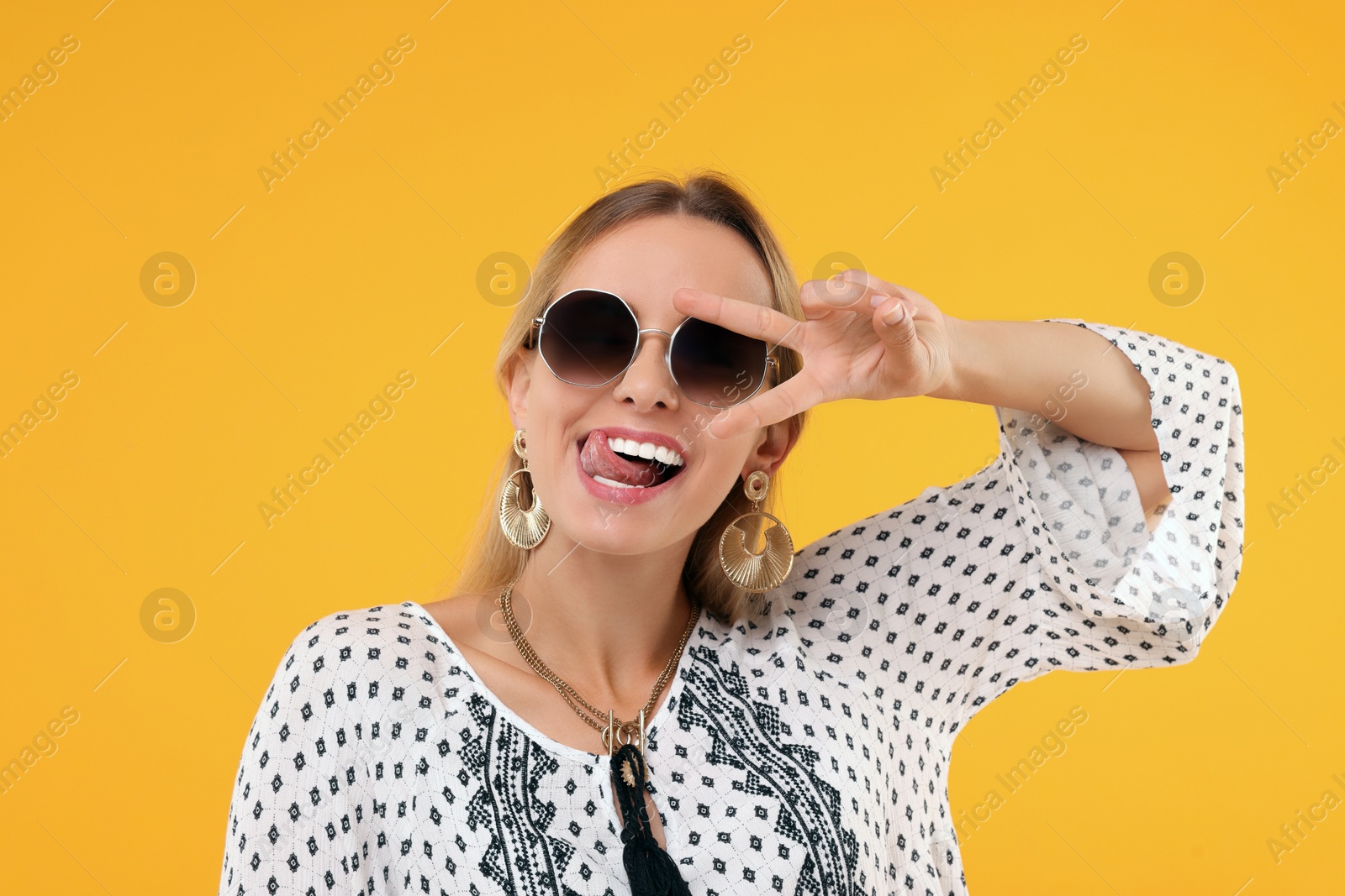 Photo of Portrait of hippie woman showing tongue and peace sign on yellow background