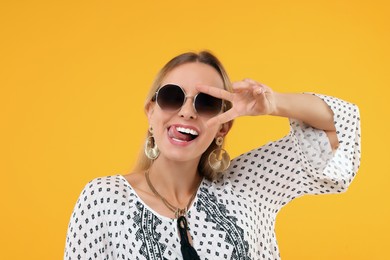 Photo of Portraithippie woman showing tongue and peace sign on yellow background