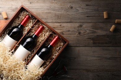 Box with wine bottles and corks on wooden table, flat lay. Space for text