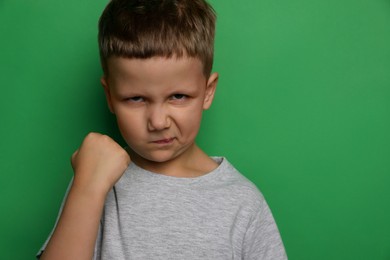 Photo of Angry little boy on green background, space for text. Aggressive behavior