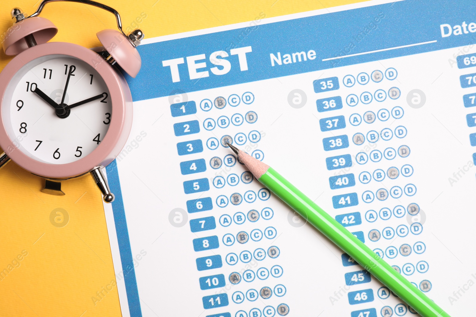 Photo of Answer sheet, pencil and alarm clock on yellow background, flat lay. Student passing exam