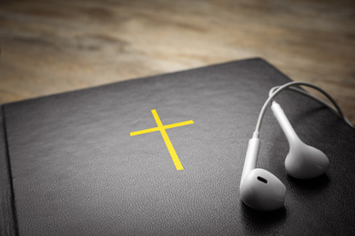 Photo of Bible and earphones on table, closeup. Religious audiobook