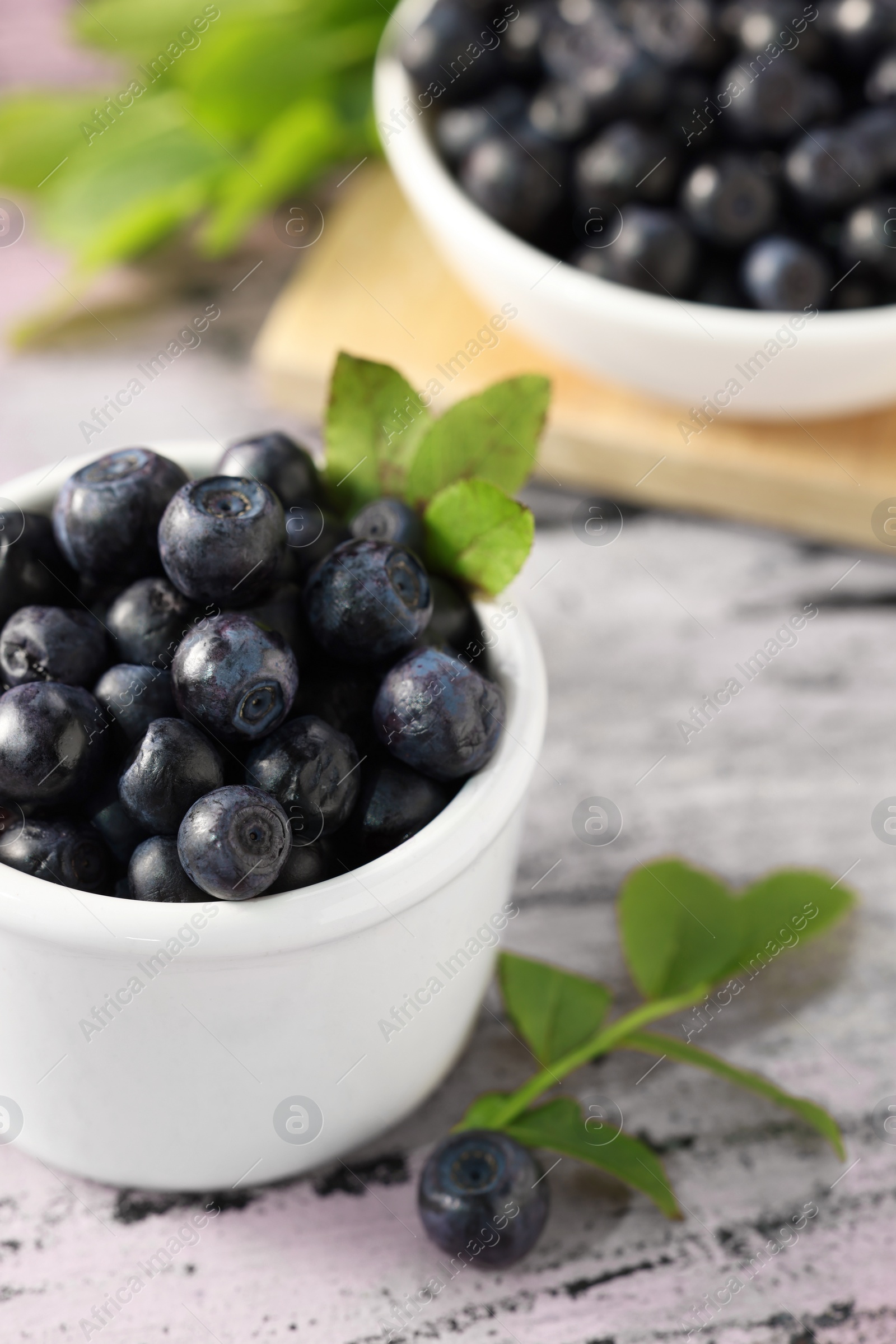 Photo of Tasty fresh bilberries with green leaves in bowls on old pink wooden table, closeup