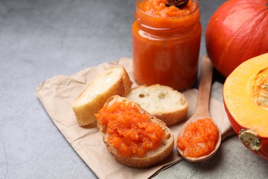 Slices of bread with delicious pumpkin jam and fresh pumpkin on grey table