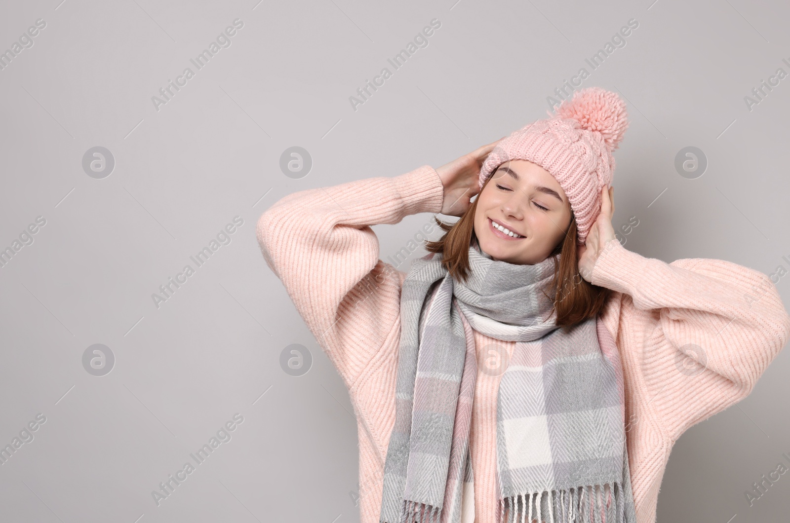 Photo of Beautiful woman in warm scarf and hat on gray background, space for text