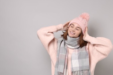 Photo of Beautiful woman in warm scarf and hat on gray background, space for text