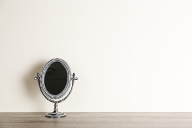 Photo of Small mirror on wooden table near light wall. Space for text