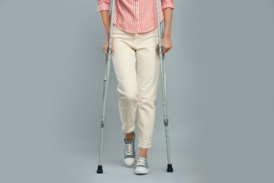 Young woman with axillary crutches on grey background, closeup