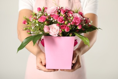 Woman holding paper gift box with flower bouquet on light background, closeup