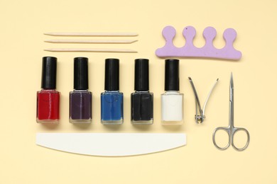 Photo of Nail polishes and set of pedicure tools on beige background, flat lay