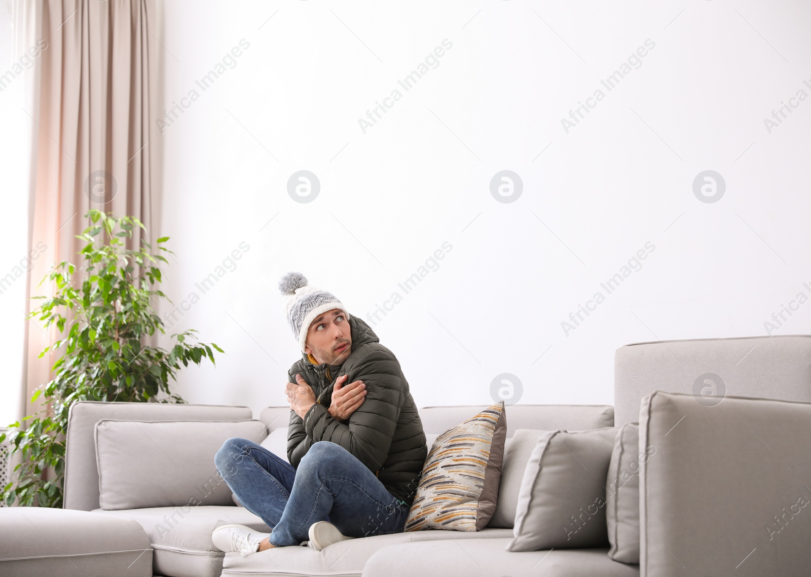 Photo of Young man wearing warm clothes freezing on sofa at home. Air conditioner malfunction