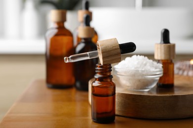 Essential oils and sea salt on wooden table in bathroom, closeup