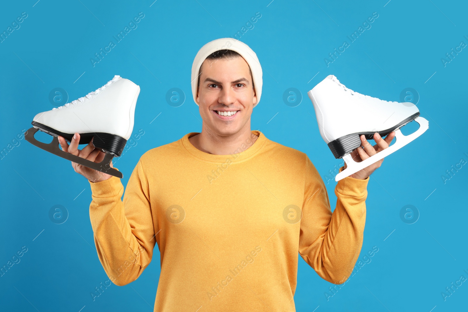 Photo of Happy man with ice skates on light blue background