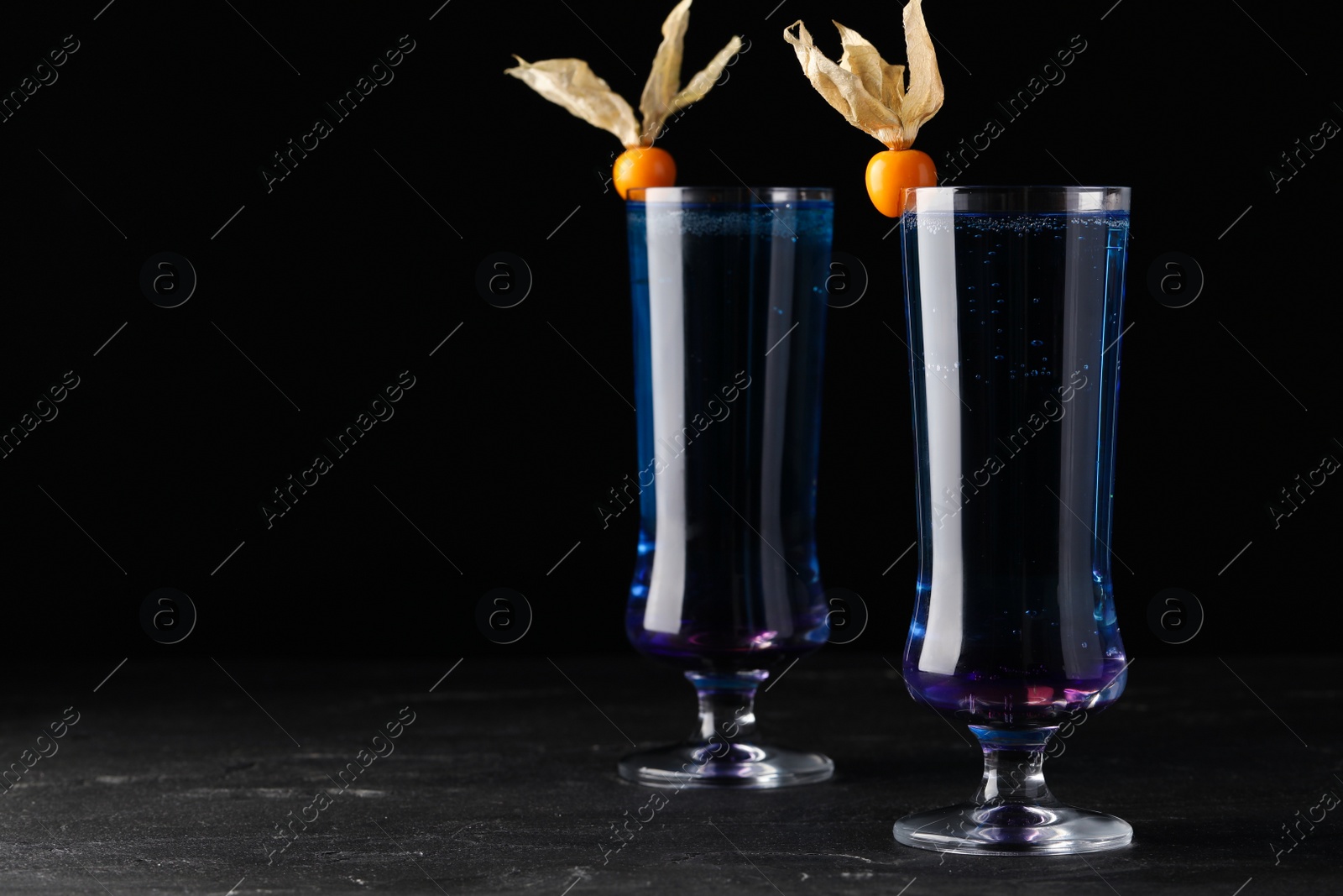 Photo of Refreshing cocktails decorated with physalis fruits on grey table against black background. Space for text