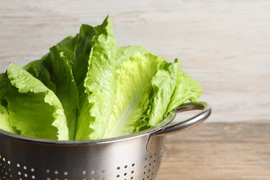 Colander with fresh leaves of green romaine lettuce on wooden background, closeup. Space for text