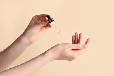 Photo of Woman dripping cosmetic oil onto hand against beige background, closeup