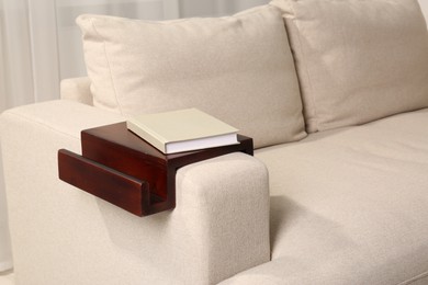 Book on sofa armrest wooden table in room. Interior element