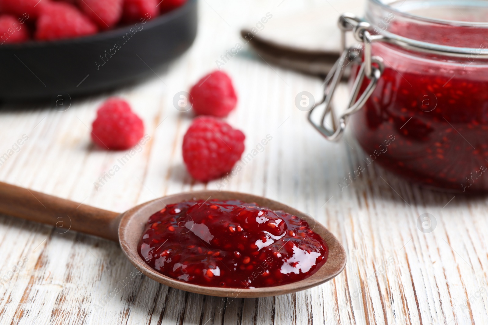 Photo of Raspberry jam in spoon on white wooden table, closeup