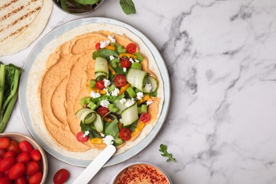 Photo of Tortilla with hummus and vegetables on white marble table, flat lay. Space for text