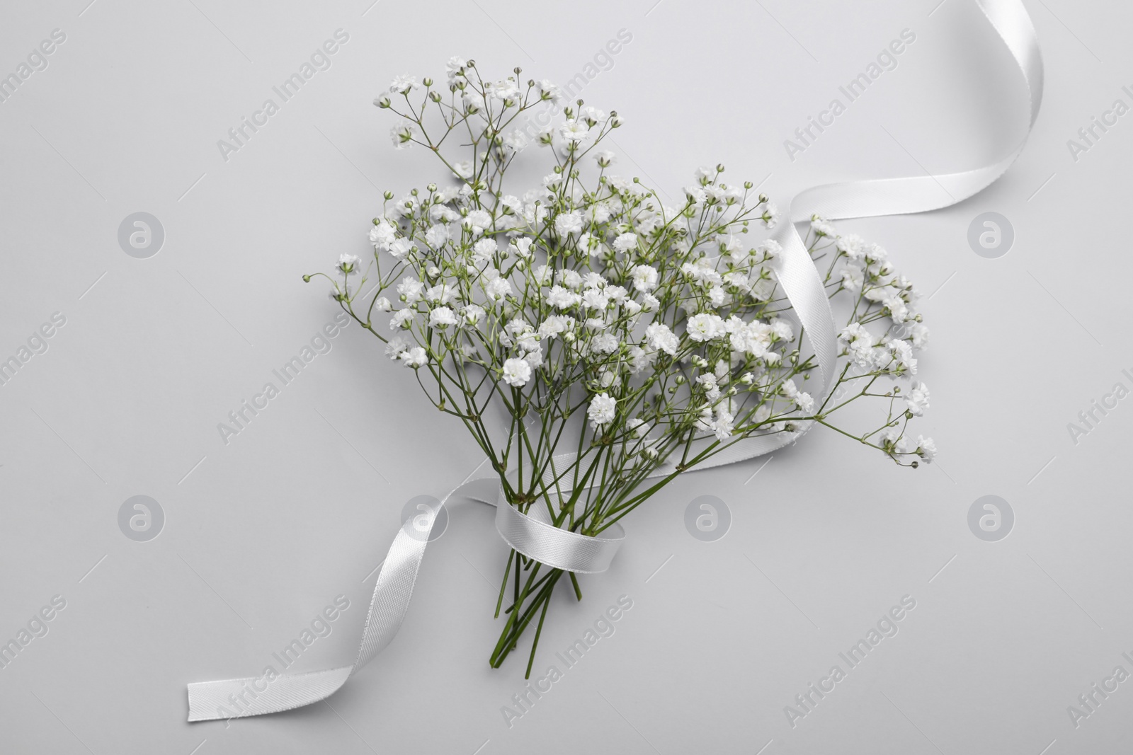 Photo of Beautiful bouquet of white gypsophila flowers with ribbon on light grey background, top view