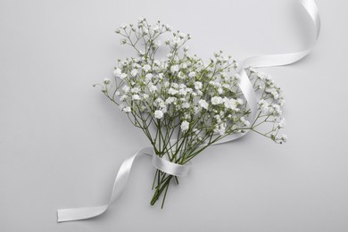 Beautiful bouquet of white gypsophila flowers with ribbon on light grey background, top view