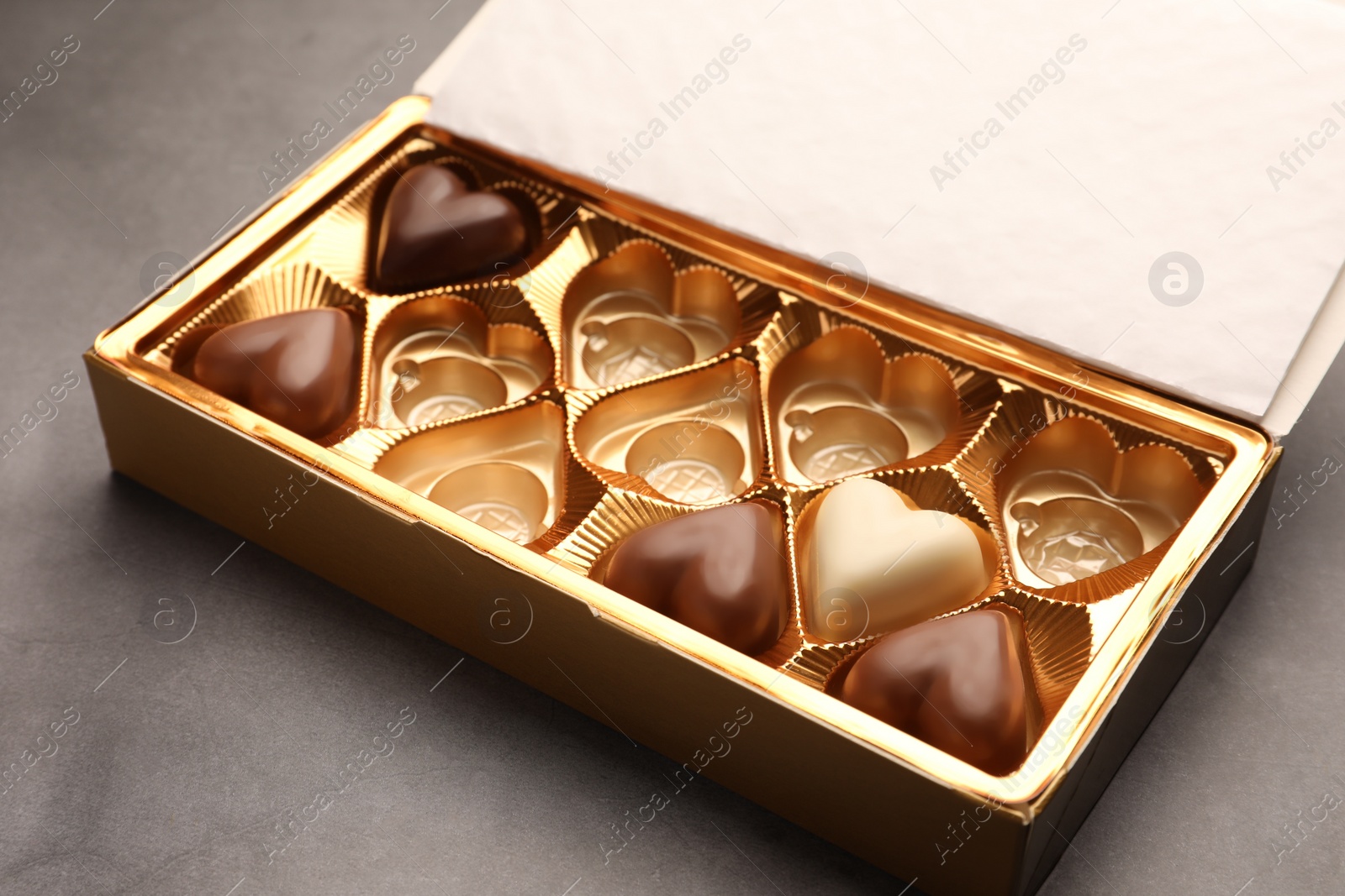 Photo of Partially empty box of chocolate candies on grey table, closeup