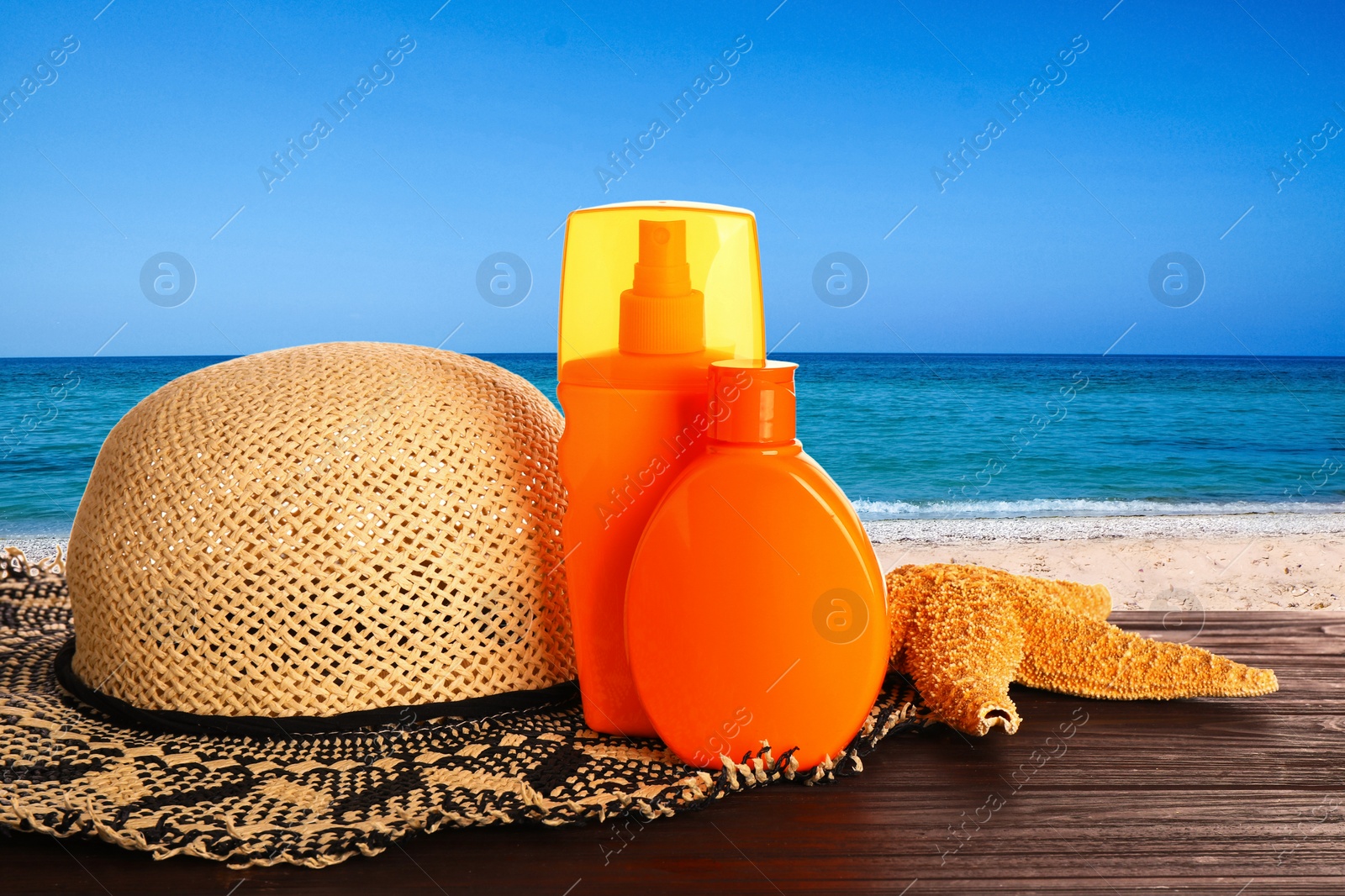 Image of Set of sun protection products and stylish hat on wooden table near sea