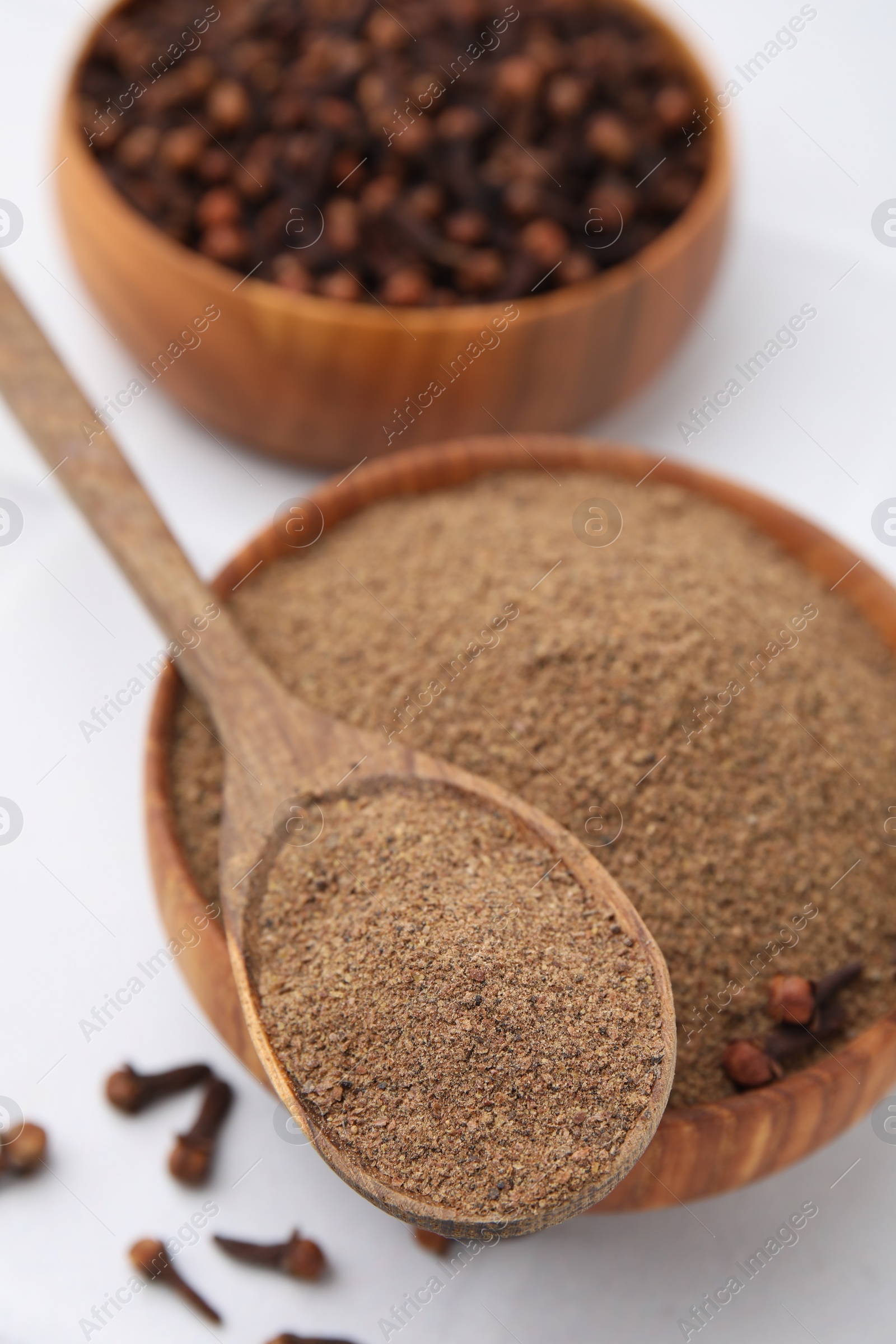 Photo of Aromatic clove powder in bowl, dried buds and spoon on white table, closeup