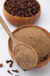 Aromatic clove powder in bowl, dried buds and spoon on white table, closeup